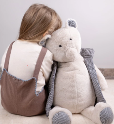 Child in brown overalls hugging MINO  bear against a plain background